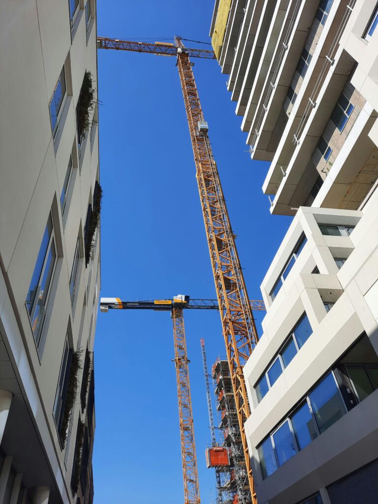 A dynamic view of modern buildings and active tower cranes against a blue sky.